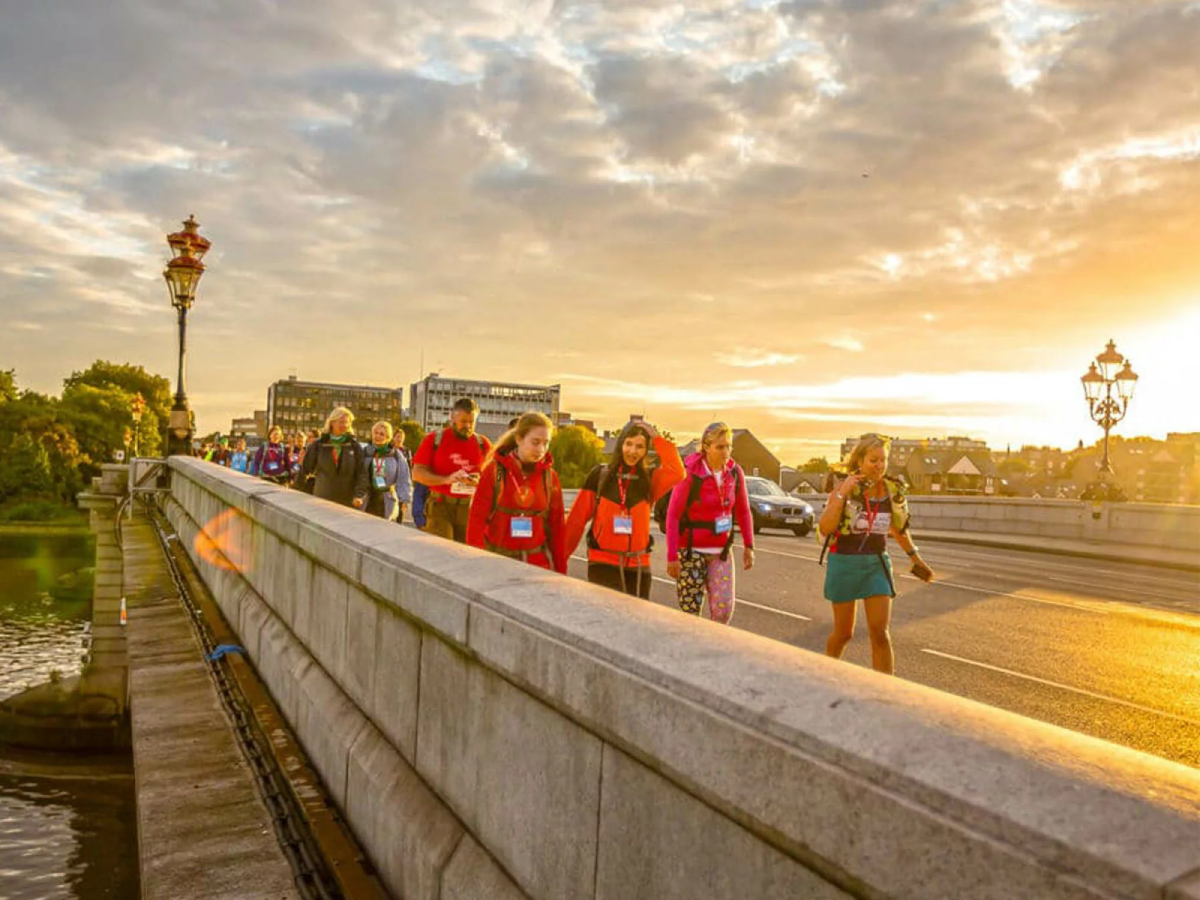 Thames Bridges Trek Participants Walking Across Bridge As Sun Goes Down