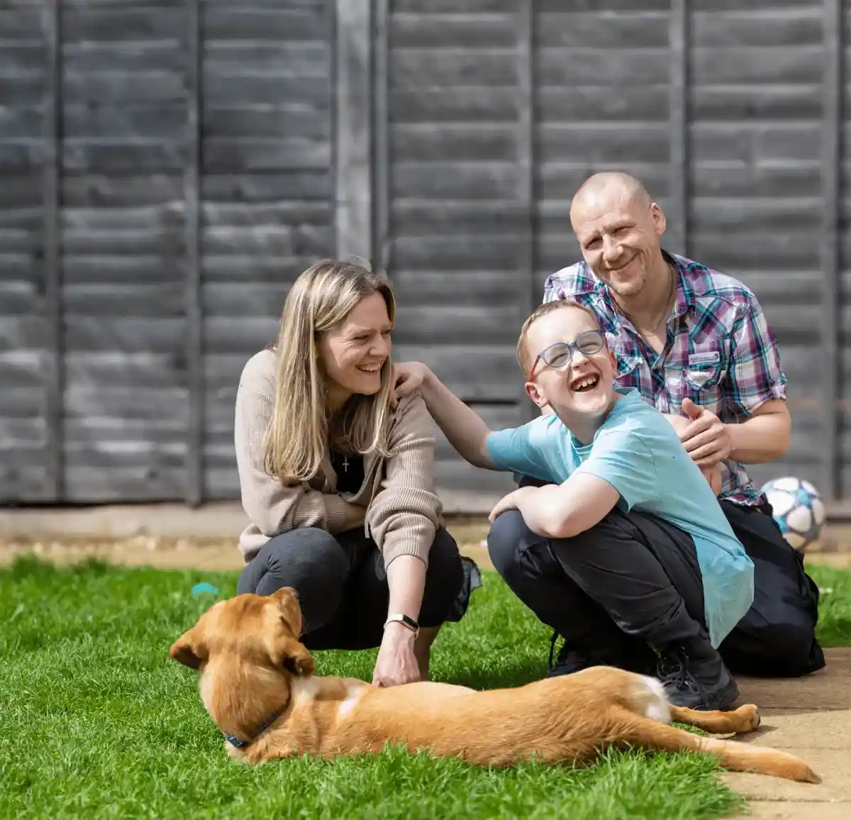Family Dog Golden Retreiver Laying Down Grass Garden Child Parents Crouched Down Smiling Closeup Frontfacing