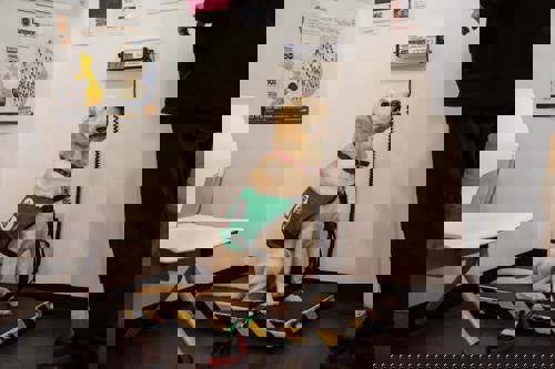 A yellow Labrador is on the scale looking up at someone who is weighing them