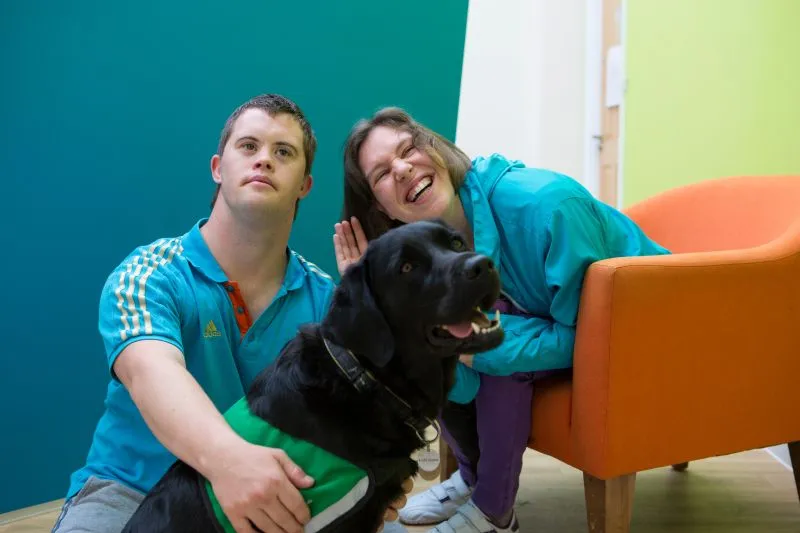 People sitting with and stroking community dog smiling and waving